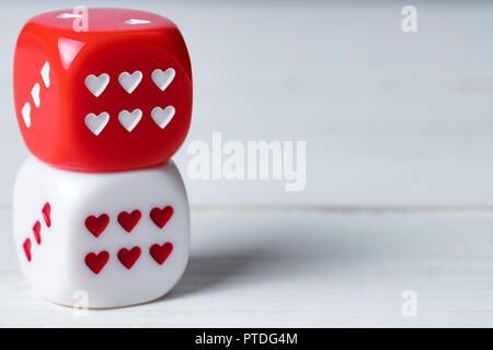 Two stacked red and white Valentines Day heart dice on wooden background. Copy space on the right. Stock Photo