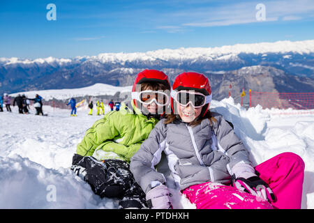Children sitting on the ski slopes playing in the snow Stock Photo