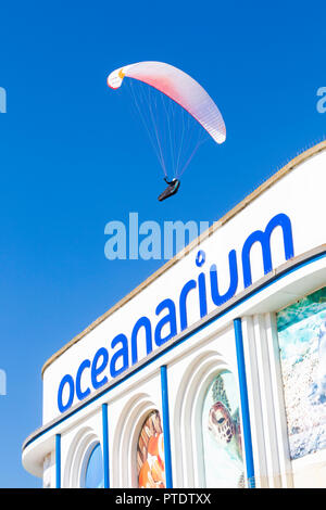 Bournemouth, Dorset, UK. 9th Oct, 2018. UK weather: unbroken blue skies and warm sunshine, as temperatures rise and visitors head to the seaside to enjoy the sun and the Indian summer. Perfect weather for paragliding and paraglider getting a birds eye view! Over the Oceanarium aquarium in Bournemouth. Credit: Carolyn Jenkins/Alamy Live News Stock Photo