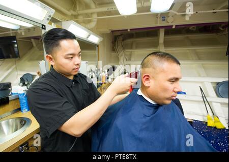 PACIFIC OCEAN (July 15, 2017) Ship’s Serviceman Seaman John Calazan, a native of Santa Barbara, California, gives a haircut to Information Systems Technician 3rd Class Paul Regina, a native of San Diego, in the barber shop aboard the amphibious assault ship USS America (LHA 6). America is currently embarked on its maiden deployment and is part of the America Amphibious Ready Group comprised of more than 1,800 Sailors and 2,600 Marines assigned to the amphibious dock landing ship USS Pearl Harbor (LSD 52), the amphibious transport dock ship USS San Diego (LPD 22) and America. Stock Photo