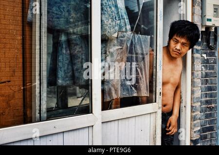 Beijing / China - JUN 24 2011: man looking outside of his home to the street in a typical city hutong Stock Photo