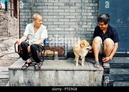 Beijing / China - JUN 24 2011: two man playing with a dog outside their home in a traditional chinese city hutong