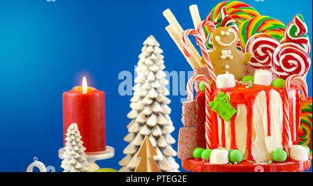 On trend festive candyland Christmas drip cake on blue background. Stock Photo