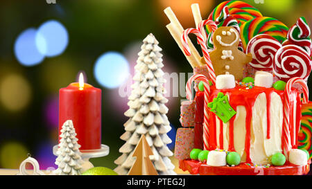 On trend festive candyland Christmas drip cake against festive Christmas tree bokeh lights background. Stock Photo