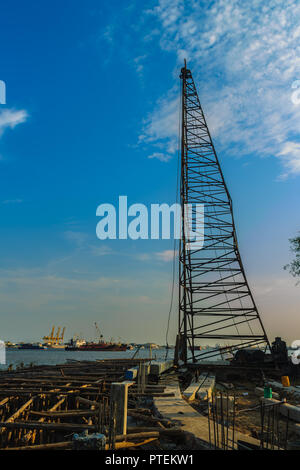 Pile driving machine with reinforced concrete piles at jetty construction site near the river against blue sky background. Stock Photo