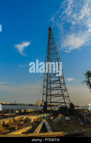 Pile driving machine with reinforced concrete piles at jetty construction site near the river against blue sky background. Stock Photo