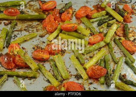 Roasted asparagus and tomato slices sprinkled with olive oil on aluminum foil on baking sheet Stock Photo