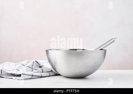 Baking concept. Bowl with a whisk and dishcloth on white marble table over pink background with copy space. Stock Photo