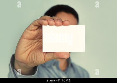 Man holding white business card on concrete wall background. businessman closes his eyes business card. Blank for text. White business card in hand. H Stock Photo