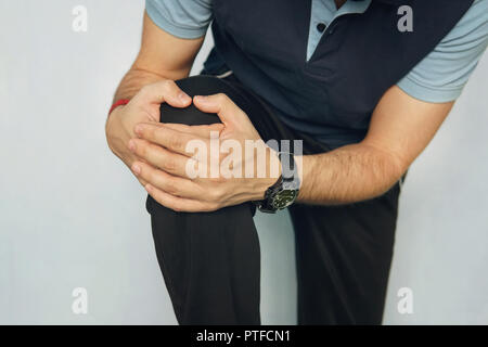 Man with knee pain on color background. young man is holding his hands over his sick knee on a blue background. athlete in a tracksuit with a pain in  Stock Photo