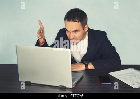 the young man freelancer programmer PC user with a disgruntled bitter angry expression on his face looking at the laptop in front of him by moving his Stock Photo
