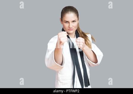 Agressive young athletic woman in white kimono with black belt wraps around the neck standing and ready to fighting. Japanese karate and sports concep Stock Photo