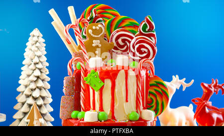 On trend festive candyland Christmas drip cake on blue background. Stock Photo