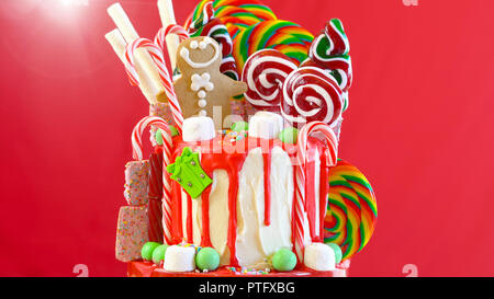 On trend festive candyland Christmas drip cake on red background. Stock Photo