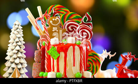 On trend festive candyland Christmas drip cake against festive Christmas tree bokeh lights background. Stock Photo