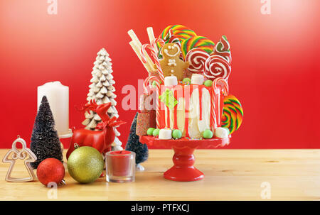 On trend festive candyland Christmas drip cake on red background. Stock Photo