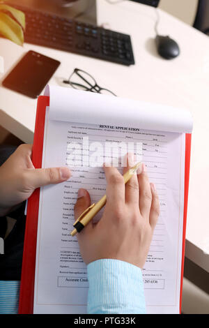 Portrait of hand on the form with pen. Picture of form on the clipboard and picture of phone, glasses, mouse and keyboard on the table. Stock Photo