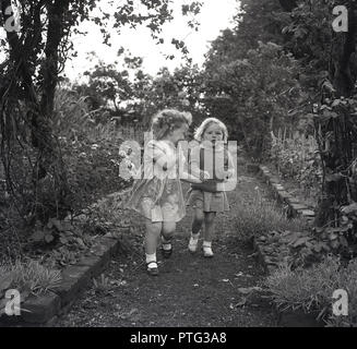 1950s, historical, two young girls, holding hands, walk along a garden path together, England, UK. Stock Photo