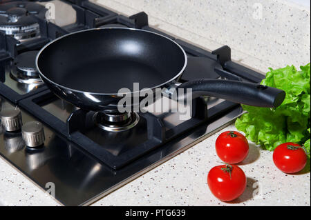 Black frying pan on a plate with tomatoes and lettuce leaves Stock Photo