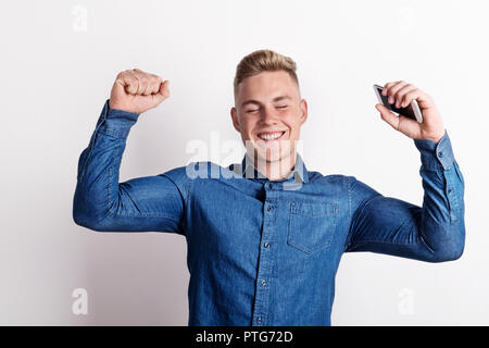 Portrait of a happy young man in a studio, holding smartphone. Stock Photo