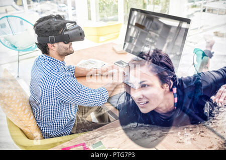 Composite image of graphic designer in virtual reality simulator while using computer Stock Photo