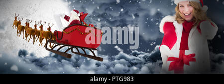 Composite image of festive blonde holding christmas gift and pointing her finger Stock Photo