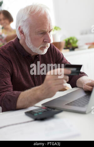 Focused senior man with credit card paying bills at laptop Stock Photo
