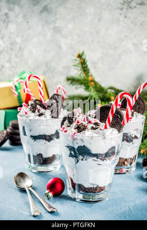 Christmas dessert, peppermint chocolate trifle in portion glasses with candy cane sweets and chocolate cookies, on light blue concrete table with xmas Stock Photo