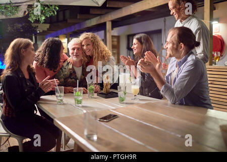 Happy friends clapping, celebrating on patio at night Stock Photo