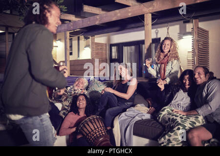 Happy friends hanging out, playing music on patio at night Stock Photo