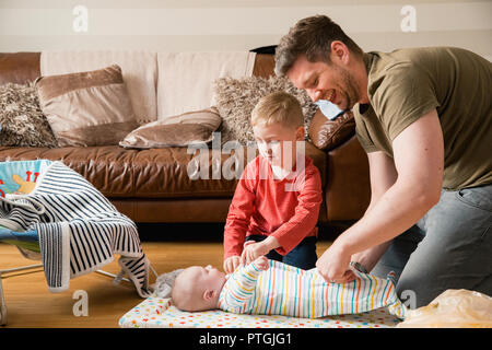 Little boy helping his father change his baby brother. They are both sitting on the floor in the living room. Stock Photo