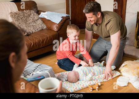 Little boy helping his father change his baby brother. They are both sitting on the floor in the living room. Stock Photo