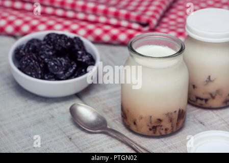 Delicious homemade natural yogurt with chopped prunes in glass jars on a white wooden table. The concept of a natural and healthy breakfast Stock Photo