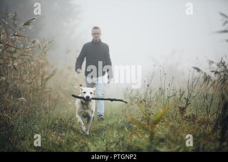 Young man playing with dog (labrador retriever) in autumn foggy morning. Stock Photo