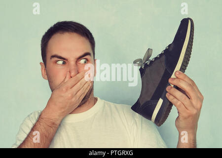 A man pinches his nostrils closed over the odor given off from the athletic shoe he is holding. Stock Photo