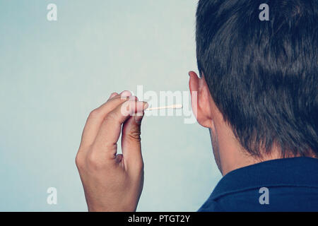 Happy man cleans his ear with a cotton swab close-up on blue background. Stock Photo