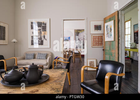 Salvaged linen sofa with artwork by Robert Rauchenberg and rustic table with 1950’s, black leather Bentwood chairs and 1920’s black basalt tea service Stock Photo