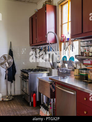 Storage in small kitchen painted traditional barn red with pots hung on twisted wire coat-hangers above cooker Stock Photo