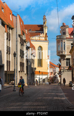 Vilnius old town, view on a summer morning of a young woman cycling along Pilies Gatve - the main thoroughfare in Vilnius Old Town, Lithuania. Stock Photo