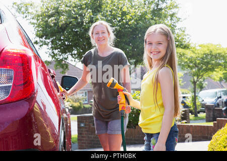 Portrait smiling mother and daughter washing car in sunny driveway