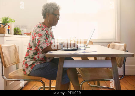 Senior woman paying bills at laptop in kitchen Stock Photo