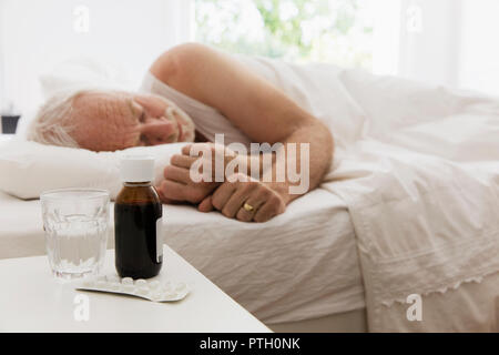 Tired senior man sleeping next to night stand with cough syrup and medicine Stock Photo