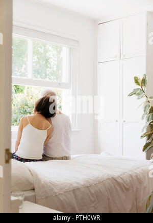 Serene senior couple sitting on bed and looking out window Stock Photo