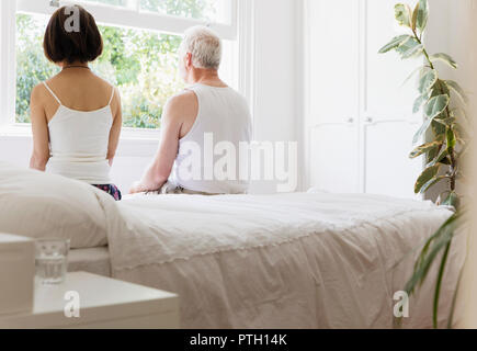 Thoughtful senior couple sitting on bed looking out window