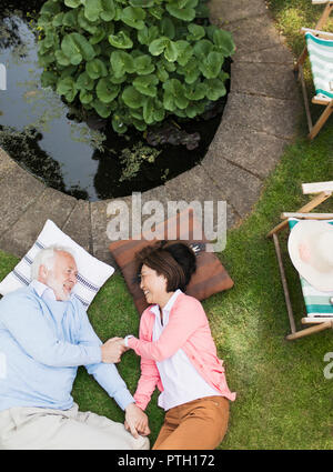 Affectionate senior couple laying by pond in garden Stock Photo