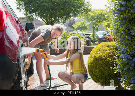 Mother and daughter washing car in sunny driveway Stock Photo