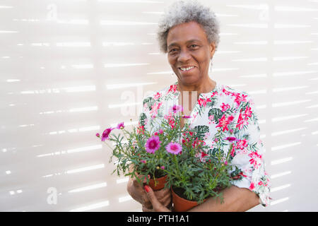 Portrait smiling, confident active senior woman gardening, holding flowerpots Stock Photo