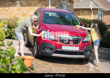 Mother and daughter washing car in sunny driveway Stock Photo