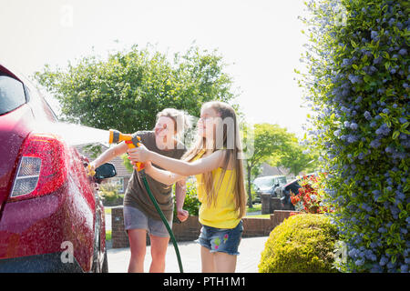 Mother and daughter washing car in sunny driveway