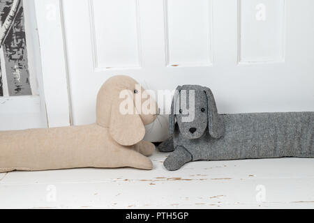 Two dog shaped draught excluders on a white painted wooden floor and in front of a door. Stock Photo